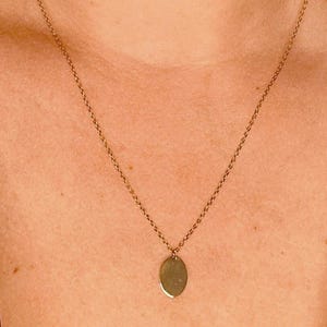 May include: A gold necklace featuring a fine chain and a small, oval pendant. The pendant hangs centrally, offering a simple and elegant appearance. This necklace is a classic piece of jewellery, suitable for everyday wear.