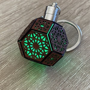May include: A wooden keychain with a geometric design and a green light inside. The keychain is shaped like a dodecahedron and has a silver metal ring.