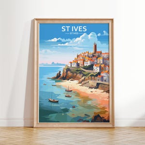 May include: A framed art print featuring a coastal town scene with the text "ST IVES". The artwork depicts a seaside village with colorful buildings, a sandy beach, and boats on the water under a blue sky.