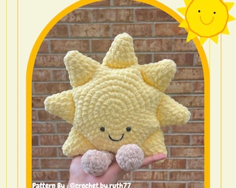May include: A handmade yellow crochet sun plushie with a smiling face and two small beige pom-poms. The text "Sunny the Sun Buddy" is at the top. The text "Pattern By: @crochet.by.ruth77" is also visible.