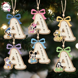 May include: Wooden Christmas ornaments shaped like the letter "A", each featuring a Disney character and a bow. The ornaments include Donald Duck, Minnie Mouse, Pluto, Daisy Duck, Mickey Mouse, and Goofy. The name "Anna" is written on each ornament.