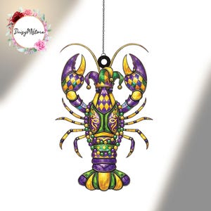 Op de afbeelding: Een Mardi Gras-thema kreeft ornament. De kreeft is versierd in paars, groen en goud, met een narrenmuts en een kralenketting. Het ornament hangt aan een zwarte ketting.