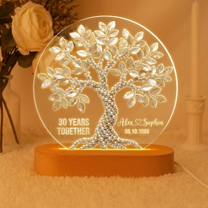 Könnte beinhalten: Ein dekoratives, beleuchtetes Baum-Ornament mit Holzsockel. Der klare Acrylkreis zeigt ein Baumdesign mit perlenartigen Akzenten und den Text "30 YEARS TOGETHER" sowie Namen mit Datum. Der Sockel strahlt ein warmes Licht aus.