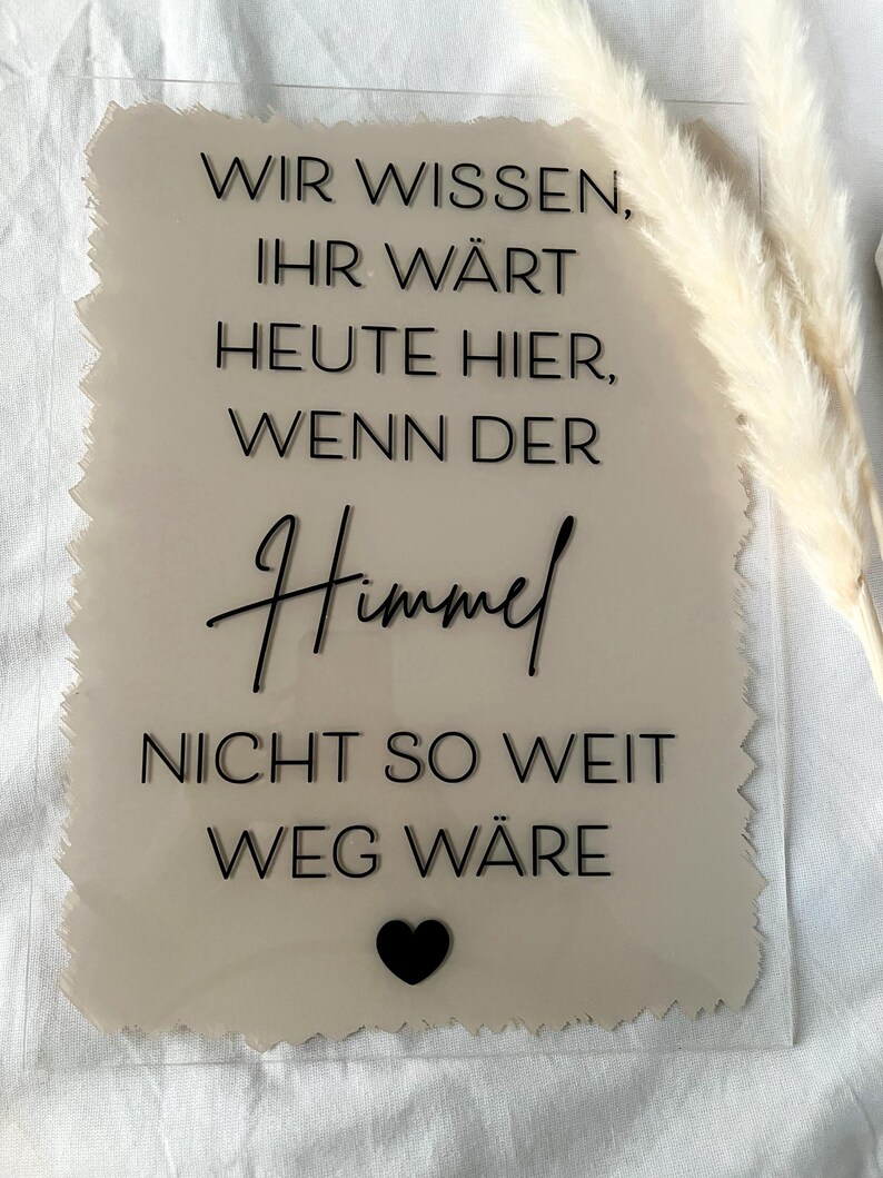 Może przedstawiać: Beżowy znak akrylowy z przetartym brzegiem i czarnym tekstem, kt&oacute;ry brzmi "Wir wissen, ihr w&auml;rt heute hier, wenn der Himmel nicht so weit weg w&auml;re". Czarne serce znajduje się na dole znaku.