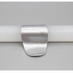 May include: A silver-colored metal clip is attached to a white cylindrical object. The clip has a curved, rectangular shape with a rounded bottom. The Chinese characters "银色" are in the upper left corner.