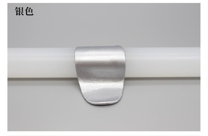 May include: A silver-colored metal clip is attached to a white cylindrical object. The clip has a curved, rectangular shape with a rounded bottom. The Chinese characters "银色" are in the upper left corner.