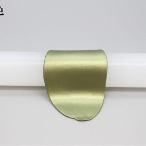 May include: A metallic, olive-green, curved object is centered on a white cylindrical form. The object has a textured surface and a rounded shape. The Chinese characters "青铜色" are in the upper left corner.