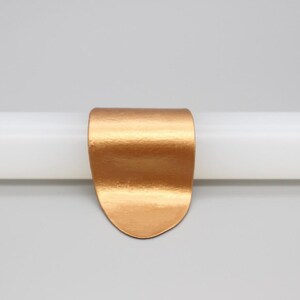 May include: A copper-colored metal clip, curved at the top and rounded at the bottom, is attached to a white cylindrical object. The clip has a textured surface. The Chinese characters "铜色" are in the top left corner.
