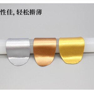 May include: Three metallic-looking, curved objects in silver, copper, and gold are displayed on a white cylindrical form. The objects have a smooth, reflective surface. Text in Chinese characters is visible at the top.