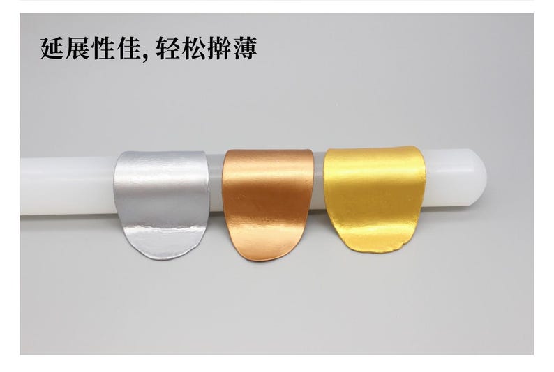 May include: Three metallic-looking, curved objects in silver, copper, and gold are displayed on a white cylindrical form. The objects have a smooth, reflective surface. Text in Chinese characters is visible at the top.