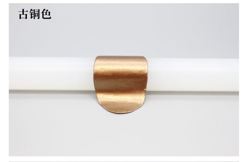 May include: A copper-colored metal clip, curved and rounded, is shown against a white background. The clip is attached to a white cylindrical object. The text "古铜色" is in the upper left corner.