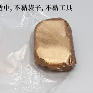 May include: A rectangular object wrapped in gold foil, resting on a crinkled, transparent plastic sheet. The object has a slightly irregular shape and a metallic sheen. Text in Chinese characters is visible.