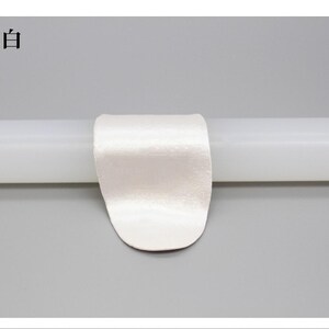 May include: A white satin ribbon is wrapped around a white cylindrical object. The text "珍珠白" is in the upper left corner. The background is a solid light gray.