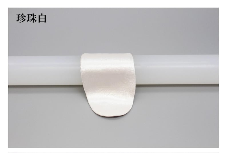 May include: A white satin ribbon is wrapped around a white cylindrical object. The text "珍珠白" is in the upper left corner. The background is a solid light gray.