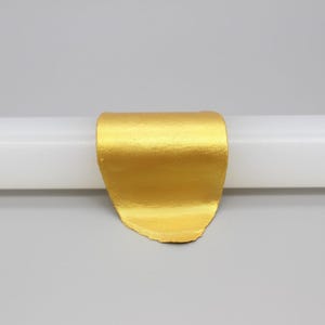 May include: A gold-colored, curved object is centered on a white cylindrical form against a gray background. The object has a textured surface and appears to be made of metal. The Chinese characters "金 色" are in the upper left corner.