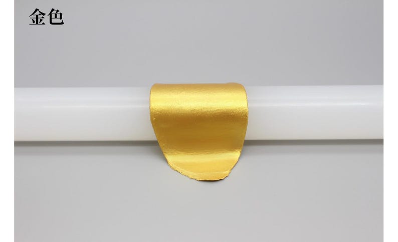 May include: A gold-colored, curved object is centered on a white cylindrical form against a gray background. The object has a textured surface and appears to be made of metal. The Chinese characters "金 色" are in the upper left corner.