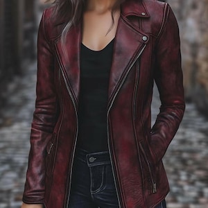 May include: A burgundy leather jacket with an asymmetrical zip, a notched collar, and zipped pockets. The jacket has a slightly distressed look and a tailored fit. The model is wearing a black top and dark wash jeans.