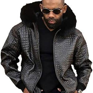 Może przedstawiać: Czarna skórzana kurtka z kołnierzem z imitacji futra. Kurtka ma teksturowany wzór przypominający krokodyla i zapięcie na zamek błyskawiczny. Osoba na zdjęciu ma na sobie okulary przeciwsłoneczne i czarną koszulkę.