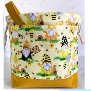 May include: A yellow drawstring bag with a gnome and bee pattern. The bag has a yellow corduroy bottom and a white drawstring.