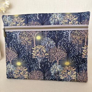 May include: A rectangular fabric pouch featuring a dark blue background with a repeating pattern of stylised trees and sunbursts in shades of yellow, light blue, and soft pink. The pouch includes a horizontal zip closure across the top.
