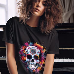 Può includere: Una maglietta nera con un design di teschio di zucchero colorato. Il teschio è circondato da un effetto di schizzi di acquerello colorato.