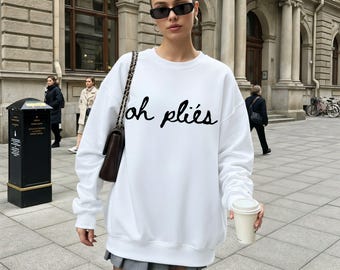 Puede incluir: Sudadera blanca con la inscripción "oh pliés" en escritura negra. La parte superior de manga larga se usa con una falda gris y gafas de sol. Un bolso marrón se lleva al hombro.