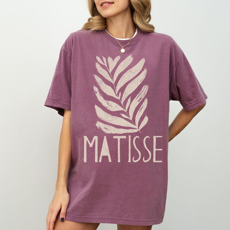 May include: A mauve oversized t-shirt with a white stylized leaf design and the text "MATISSE" printed on the front.