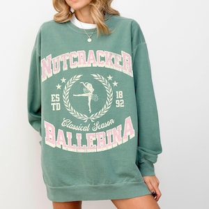 May include: A green sweatshirt with a pink graphic print that says "Nutcracker Classical Season Ballerina". The graphic also features a ballerina in a wreath.
