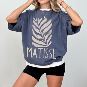 May include: A blue oversized t-shirt with a white stylized leaf design and the word "MATISSE" printed in white.