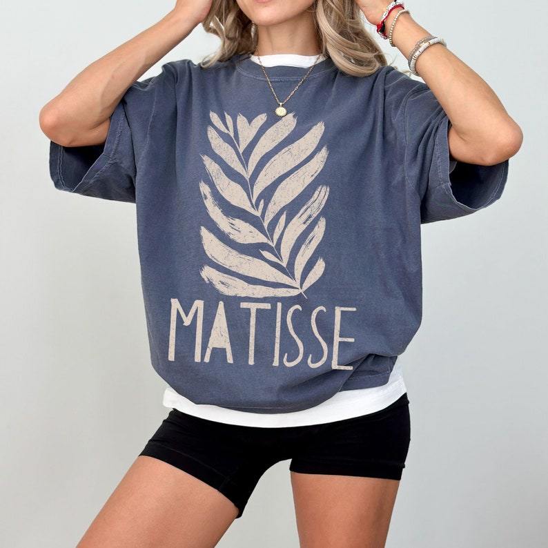 May include: A blue oversized t-shirt with a white stylized leaf design and the word "MATISSE" printed in white.