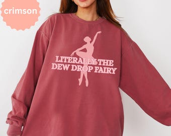 May include: A crimson long-sleeve crewneck sweatshirt featuring a light pink graphic of a ballerina in a tutu. The text "LITERALLY THE DEW DROP FAIRY" is printed in light pink block lettering across the center, with the word "crimson" in a circle.