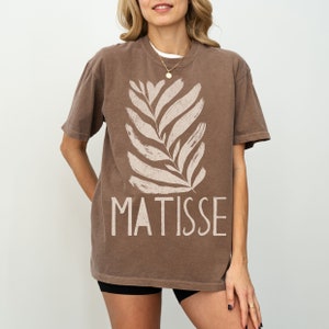 May include: A brown t-shirt with a white stylized leaf design and the text "MATISSE" printed on the front.