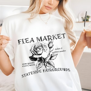 May include: White t-shirt with a black graphic design that says "Flea Market" with a rose and the text "indoor & outdoor vendors" and "new goods every week" and "Stateside Fairgrounds".