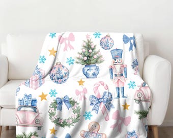 Puede incluir: Una manta de forro polar blanca con un patrón repetitivo de adornos navideños rosas y azules, bastones de caramelo, un hombre de jengibre, un cascanueces, un árbol de Navidad y un Volkswagen Beetle rosa.