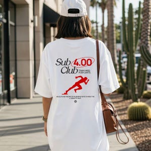 Puede incluir: Camiseta blanca con el texto "Sub 4.00 Club" en negro y rojo. La camiseta presenta un gráfico rojo de un corredor y las palabras "Train Hard, Push Limits". La camiseta también tiene el texto "Una red de élite de corredores que persiguen la milla de 4 minutos."