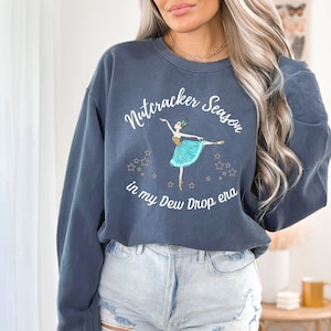 May include: A navy blue sweatshirt with the text "Nutcracker Season in my Dew Drop era" and a graphic of a ballerina in a blue tutu with gold stars.
