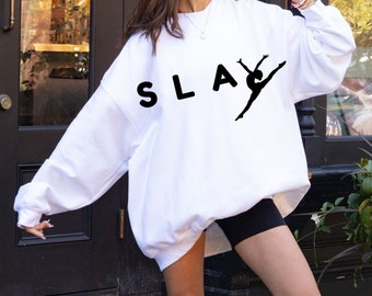 Puede incluir: Sudadera blanca con la palabra "SLAY" impresa en letras negras y una silueta de una bailarina en posición de splits.