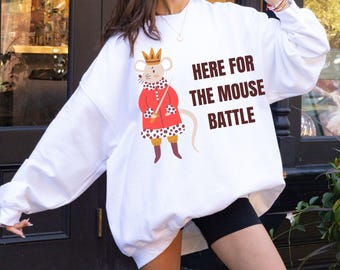 May include: White sweatshirt with a cartoon mouse wearing a crown and red coat, holding a sword. Text on the shirt reads "HERE FOR THE MOUSE BATTLE". The sweatshirt has long sleeves.