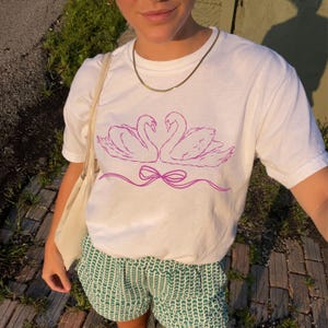 Camiseta gráfica elegante com estampa de amor de cisne, camiseta de bailarina, roupa de bailarina, roupa de lago dos cisnes, roupa de dança da moda, camiseta com laço rosa com estética coquete