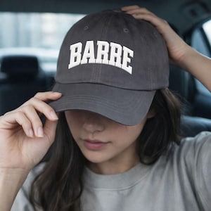 May include: A charcoal gray baseball cap with the word "BARRE" embroidered in white block letters across the front. The cap has a curved brim and a classic six-panel design.
