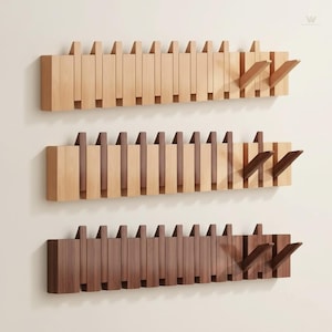 Op de afbeelding: Drie houten kapstokken in verschillende bruintinten zijn aan een muur bevestigd. Elke kapstok heeft een reeks verticale lamellen en twee schuine haken. De bovenste kapstok is lichtbruin, de middelste is bruin en de onderste is donkerbruin.