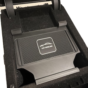 May include: Black car wireless charging pad with a textured surface, designed to fit inside a car's center console. The pad has a white logo and the text "CAR WIRELESS".