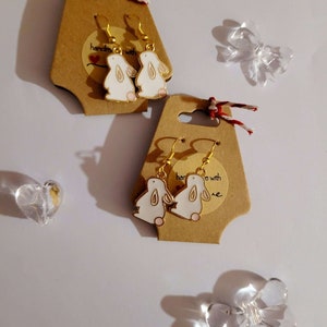 Könnte beinhalten: Ein Paar goldene Hasenohr-Ohrringe auf einer braunen Karte mit dem Text "Handgefertigt mit Liebe".