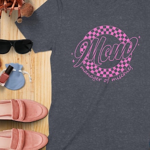May include: A dark gray t-shirt with a pink checkered circle and the text "Mom manager of mischief".