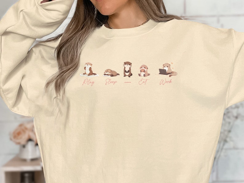 cute funny otters in a row side by side doing daily activities, play, sleep, eat, work, except for one which just stares blankly at you and a ''....' is used to describe it on a sweatshirt