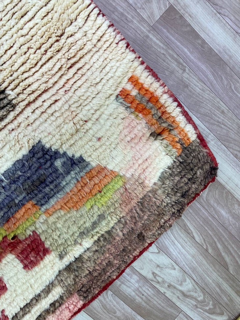 Puede incluir: Una alfombra colorida tejida a mano con un patr&oacute;n geom&eacute;trico en tonos de rojo, naranja, amarillo, verde, azul y marr&oacute;n. La alfombra tiene una textura gruesa y esponjosa y est&aacute; hecha de lana.