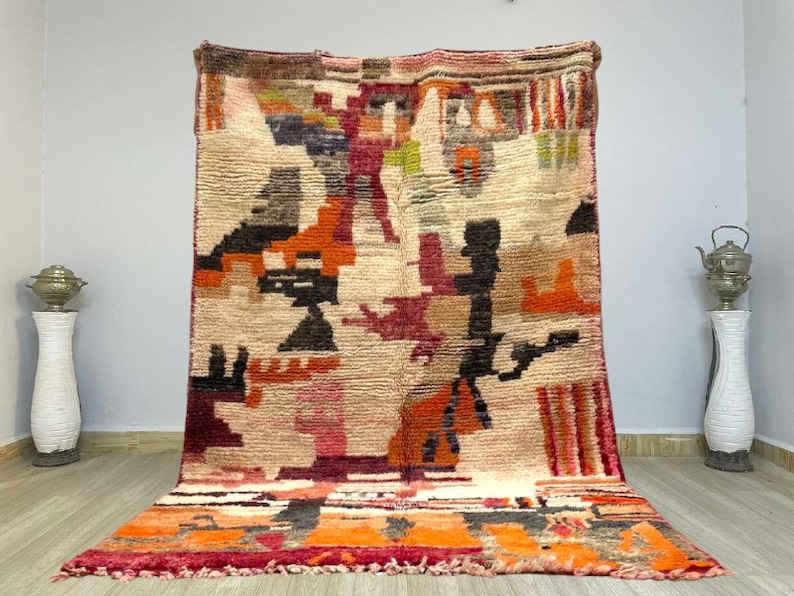 Puede incluir: Una alfombra marroqu&iacute; colorida con patrones geom&eacute;tricos en tonos rojos, naranjas, marrones y blancos. La alfombra tiene una textura tejida a mano y un borde de flecos.