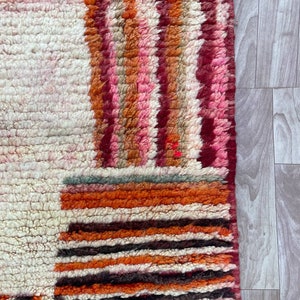 Puede incluir: Primer plano de una alfombra marroqu&iacute; colorida con fondo blanco y patrones geom&eacute;tricos en tonos rojos, naranjas, rosas y marrones.