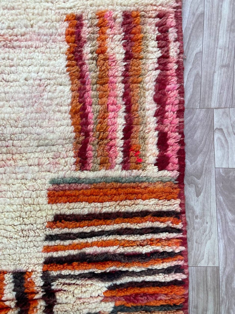 Puede incluir: Primer plano de una alfombra marroqu&iacute; colorida con fondo blanco y patrones geom&eacute;tricos en tonos rojos, naranjas, rosas y marrones.