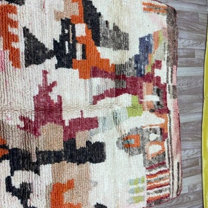Puede incluir: Una alfombra vintage tejida a mano con un patr&oacute;n geom&eacute;trico en tonos de rojo, naranja, marr&oacute;n y blanco. La alfombra tiene un aspecto desgastado y descolorido, lo que a&ntilde;ade a su car&aacute;cter &uacute;nico.